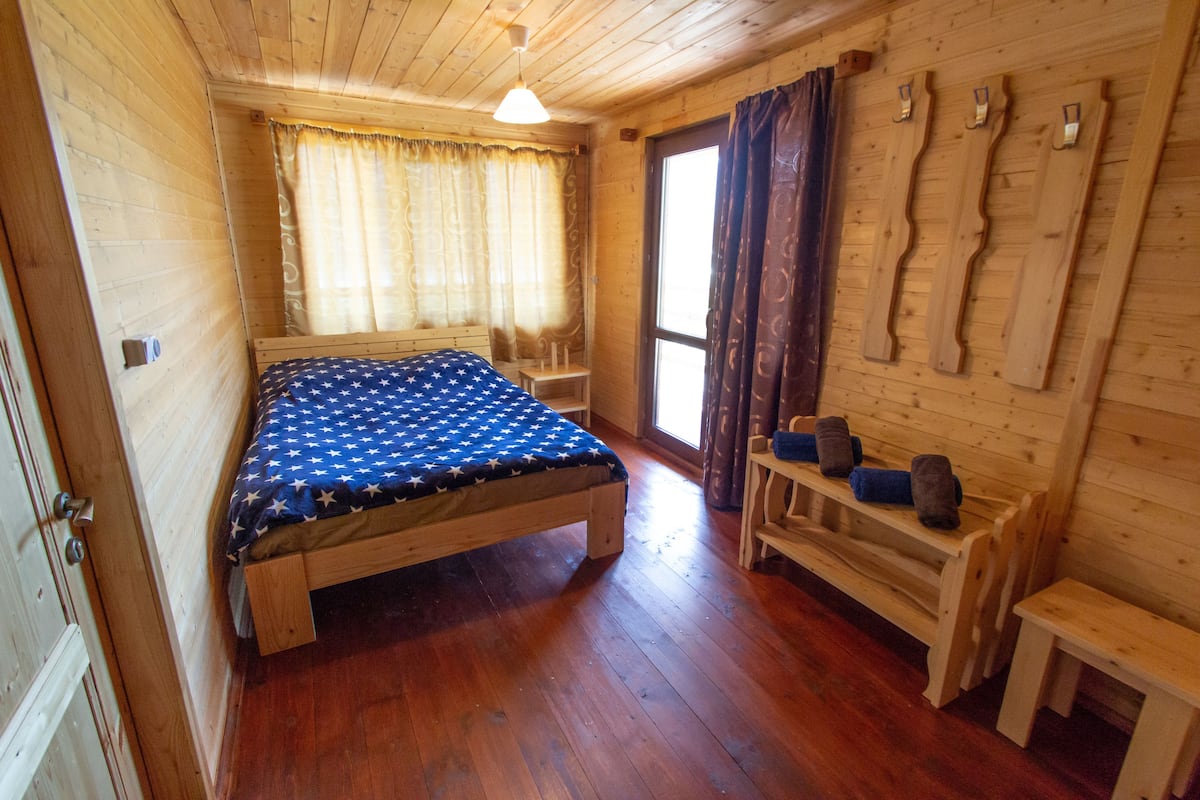 A wooden cabin room with a bed, a bench, and a small table.