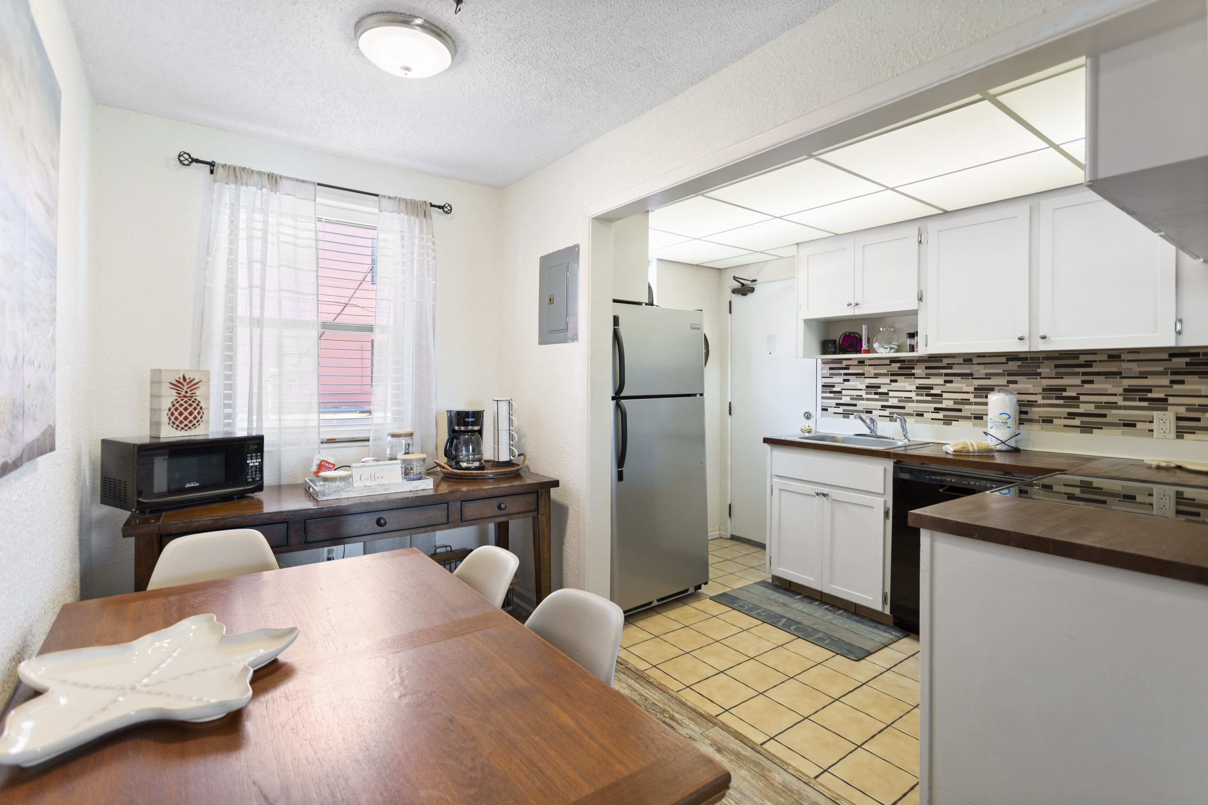 A compact kitchen with white cabinets, a stainless steel refrigerator, a microwave, and a coffee maker.