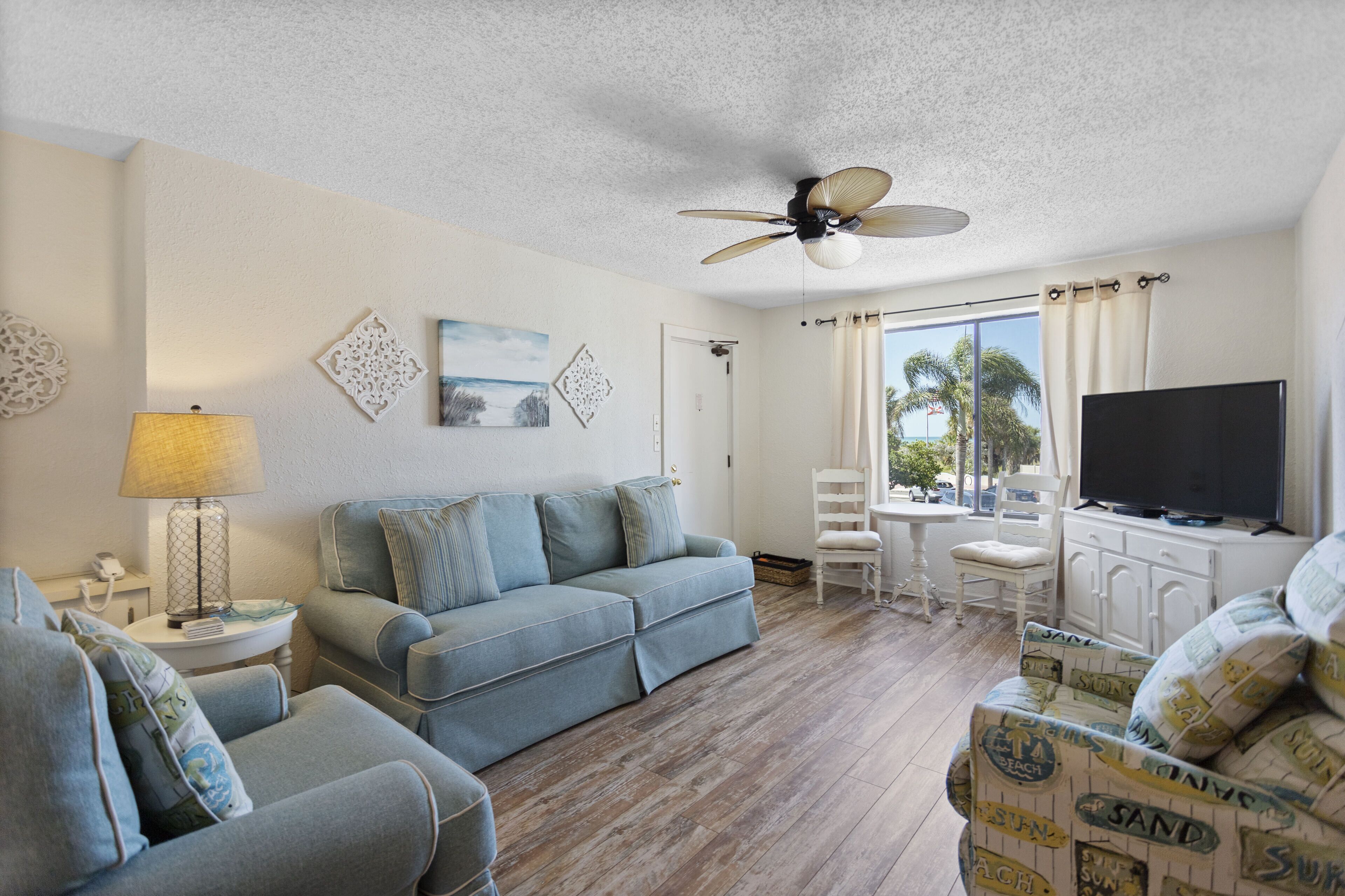 A living room with a sofa, armchairs, a TV, and a ceiling fan.