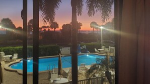 Ein Swimmingpool mit Liegestühlen und Sonnenschirmen, umgeben von Palmen und Blick auf den Sonnenuntergang.
