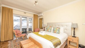 A hotel room with a large bed, a wooden bench, a small table, and a chair. - Vibrant and Safe 2 Bedroom Apartment (Cape Town)