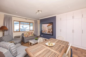 A living room with a sofa, a dining table, and a large window.