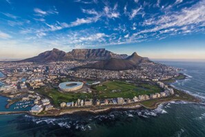 An aerial view of a coastal city with a prominent mountain, a stadium, and a harbor.