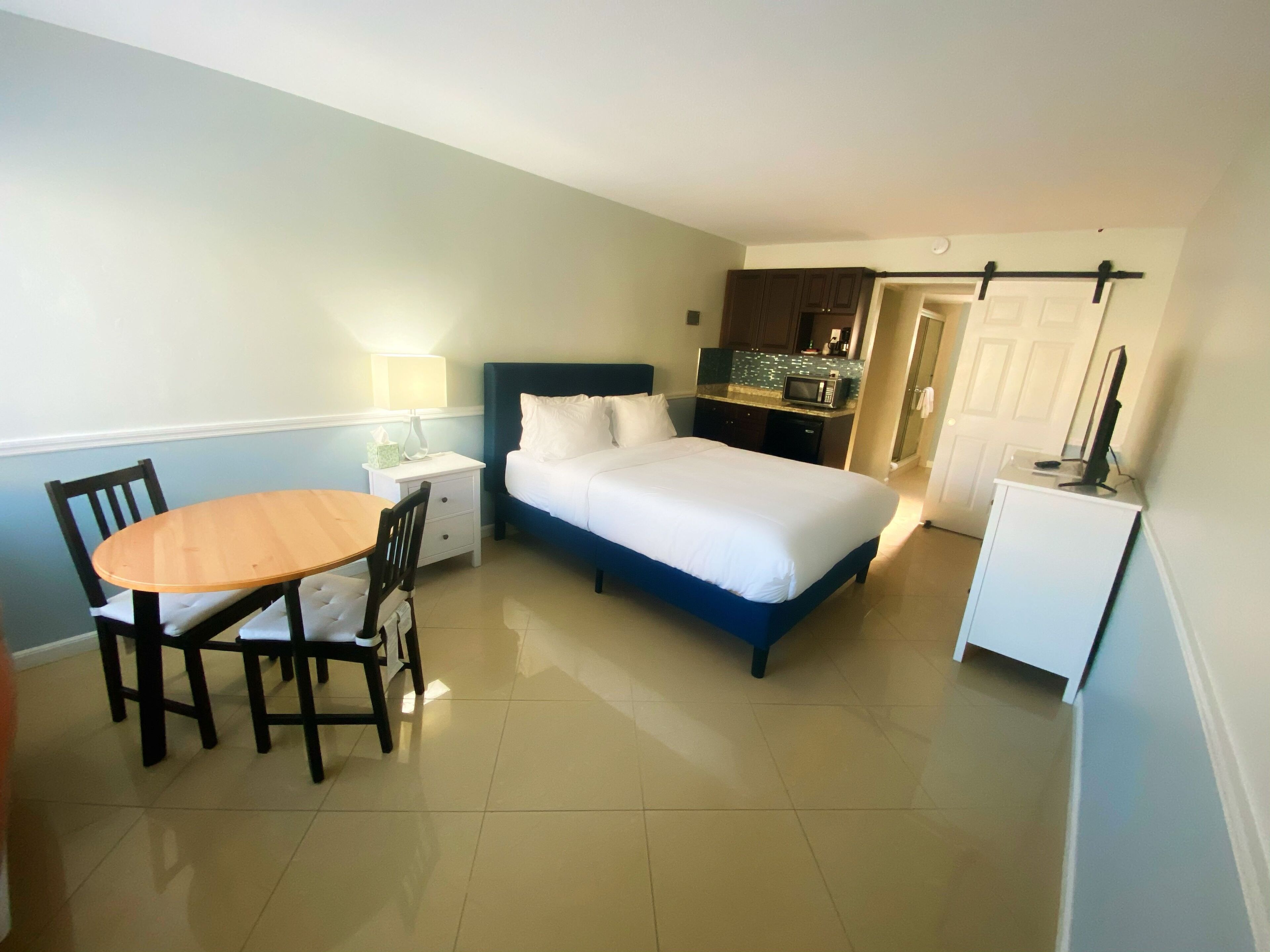 Ein Schlafzimmer mit Bett, Schreibtisch und Stuhl. Im Hintergrund ist eine Küchenzeile erkennbar.
