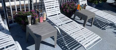 Terrasse mit weißen Metallstühlen und Tischen, umgeben von Topfpflanzen und Sonnencreme.