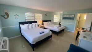 A hotel room with two beds, a desk, a chair, and a small table. - Honu Cove (Age 16+) (Deerfield Beach)