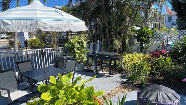 An outdoor patio with a table and chairs, surrounded by potted plants and a grill. - Honu Cove (Age 16+) (Deerfield Beach)