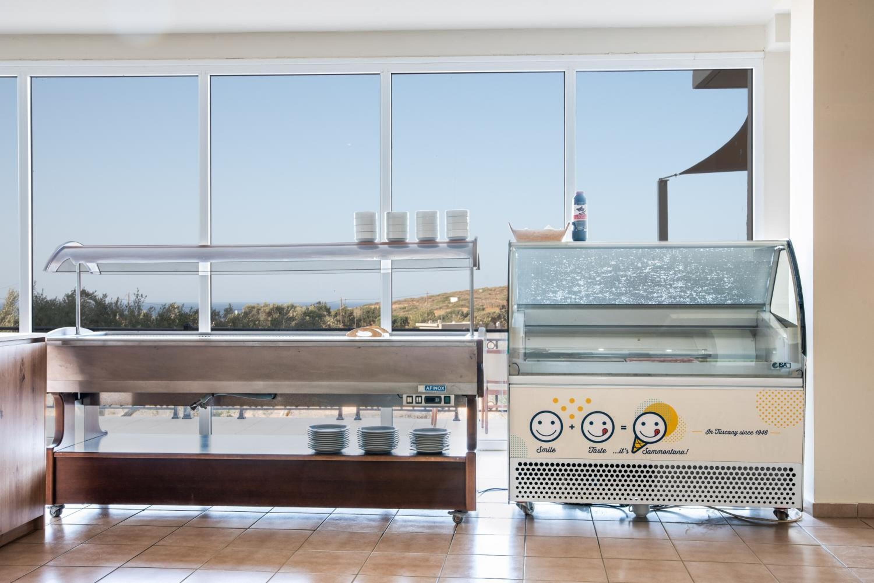 A buffet area with a glass display case and a counter with plates and cups.
