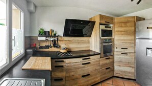 Een kleine keuken met een zwart aanrecht, houten kastjes, een inbouwoven en een roestvrijstalen koelkast.