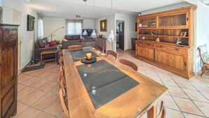 Een ruime woonkamer met een houten eettafel, een bank en een keukenhoek met een houten kastje.