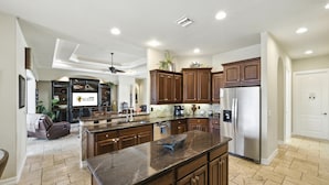 A spacious kitchen with dark wooden cabinets, a large island, and a stainless steel refrigerator. - 4BR gulf access villa w/heated pool & hot tub! Villa Francesca - SWFL Rentals (Cape Coral)