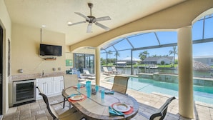 A dining area with a table, chairs, and a TV mounted on the wall. - 4BR gulf access villa w/heated pool & hot tub! Villa Francesca - SWFL Rentals (Cape Coral)