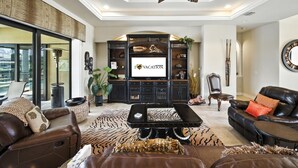 A spacious living room with a large flat-screen TV, leather sofas, a coffee table, and a ceiling fan. - 4BR gulf access villa w/heated pool & hot tub! Villa Francesca - SWFL Rentals (Cape Coral)
