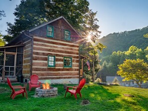Eine Blockhütte mit Feuerstelle und roten Stühlen im Garten.