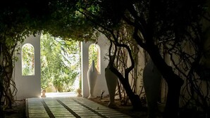 A pathway leading to a structure with arched windows, surrounded by trees and vases. - Villa HEIWA - havre de paix (Hammamet)