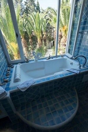 A bathroom with a bathtub, a window, and a view of palm trees.