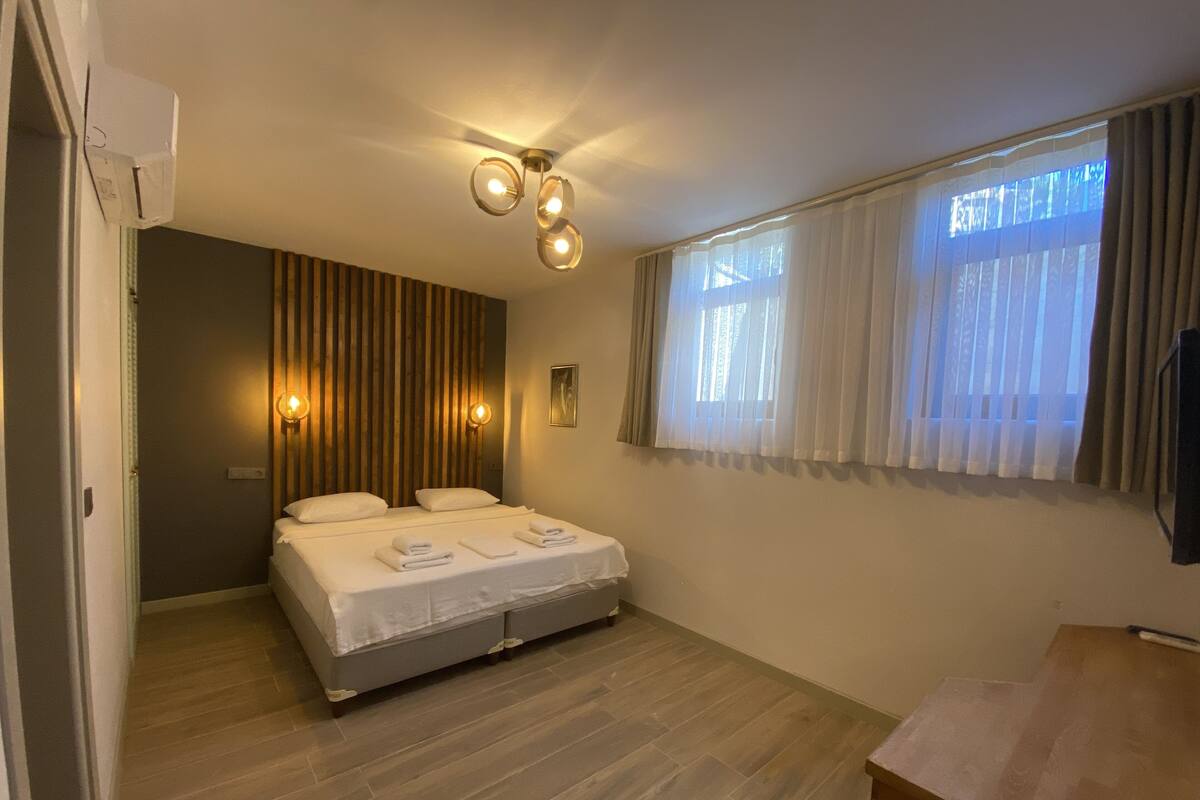 Hotelkamer met een bed, een wand van houten latten, een plafondlamp en een raam met gordijnen.