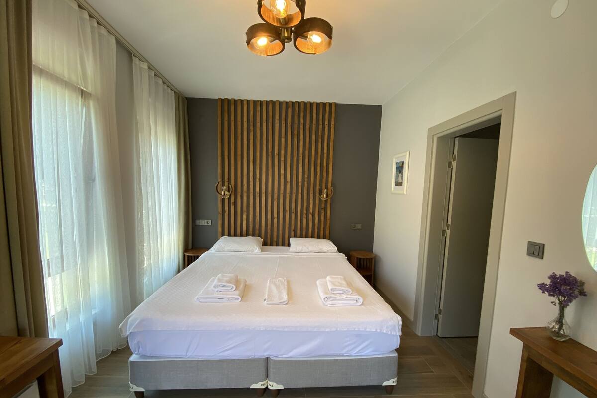 Hotelkamer met een groot bed, houten hoofdbord, nachtkastje, wandlamp en een deur.