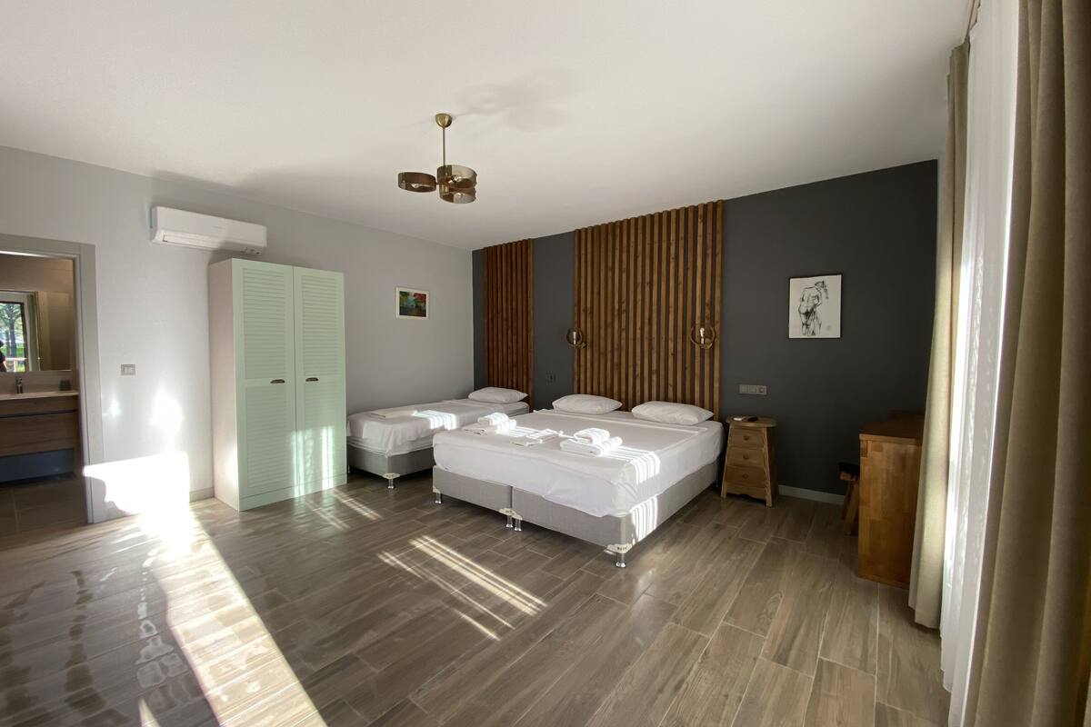 Een moderne slaapkamer met twee bedden, een houten hoofdbord, een plafondlamp en een klein houten nachtkastje.