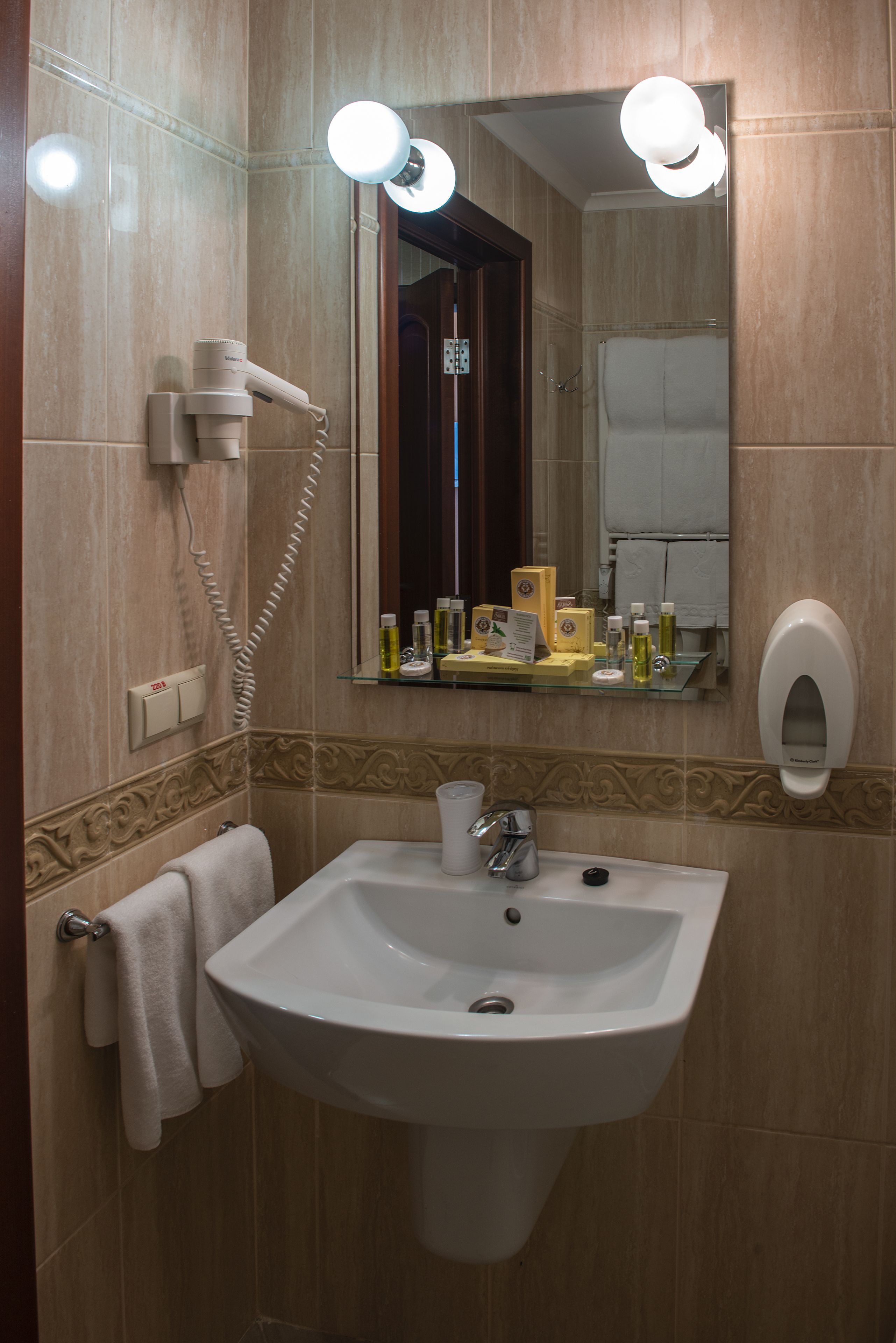 Une salle de bain équipée d’un lavabo, d’un miroir, d’un porte-serviettes et d’un sèche-cheveux fixé au mur.
