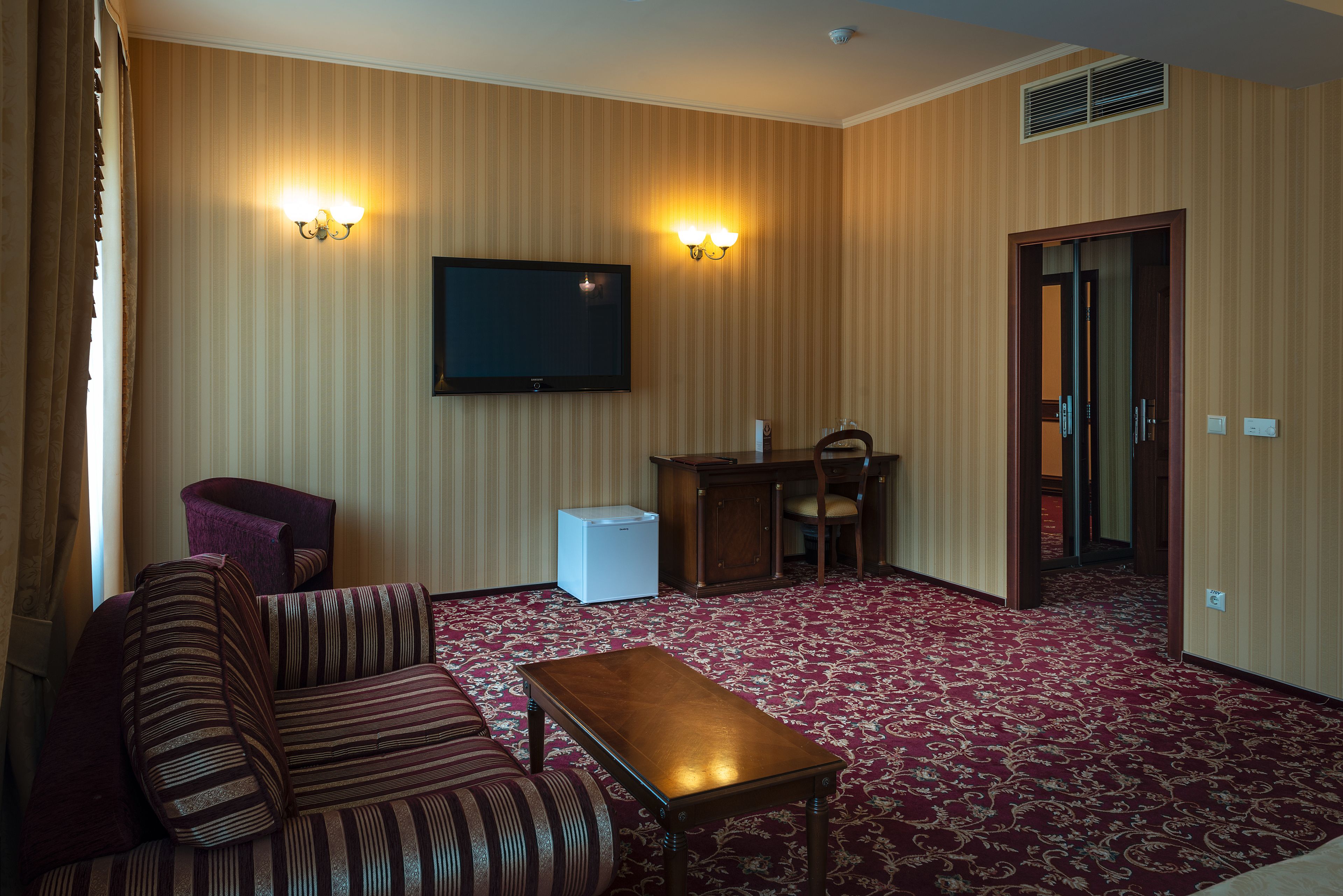 A hotel room with a sofa, a small table, a television, and a desk with chairs.