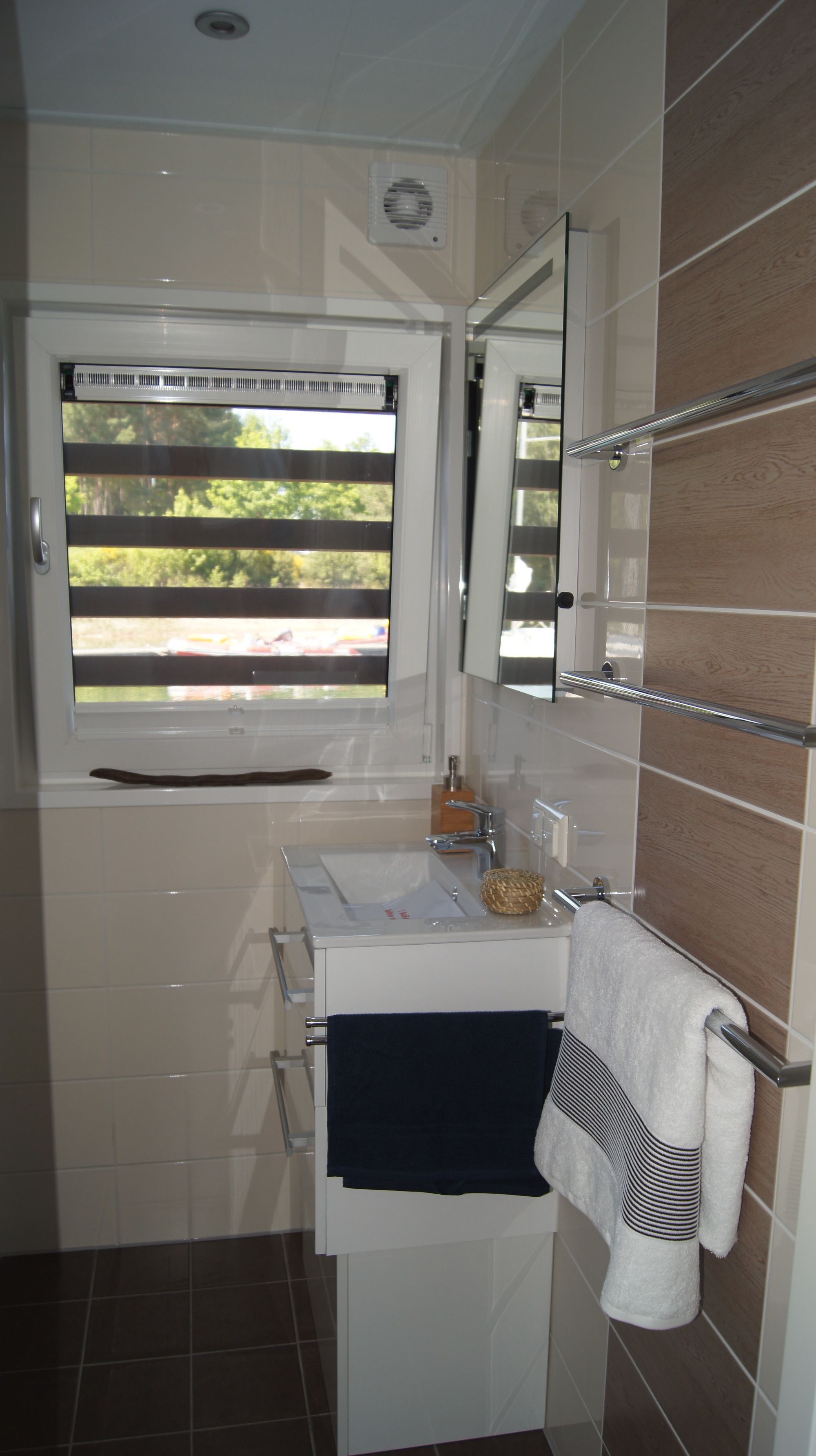 A bathroom with a window, a sink, a mirror, and a towel rack.
