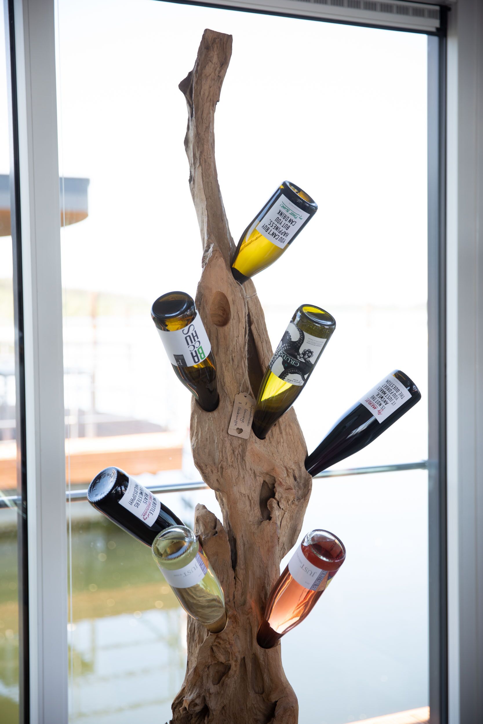 Una dispensa in legno con diverse bottiglie di vino davanti a una finestra.