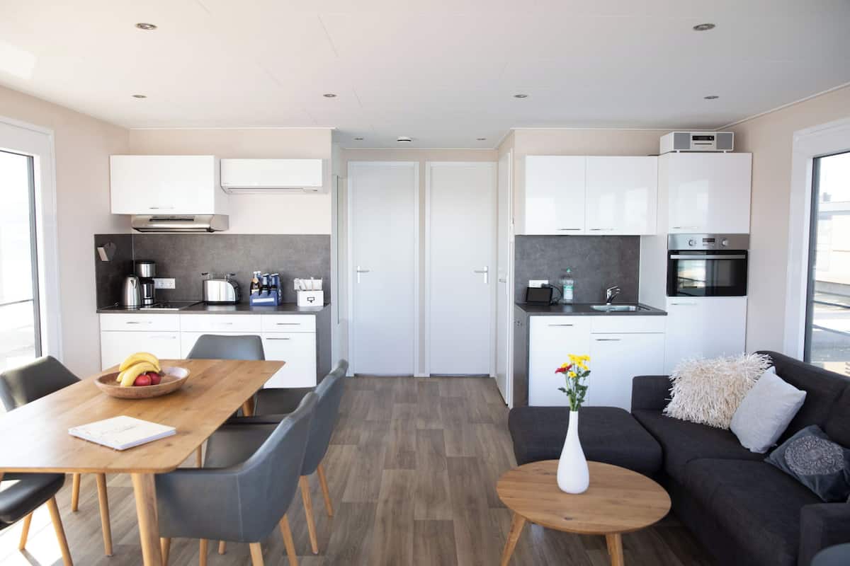 A modern kitchen with white cabinets, a dining area with a wooden table and chairs, and a living area with a sofa and a coffee table.