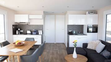 A modern kitchen with white cabinets, a dining area with a wooden table and chairs, and a living area with a sofa and a coffee table.