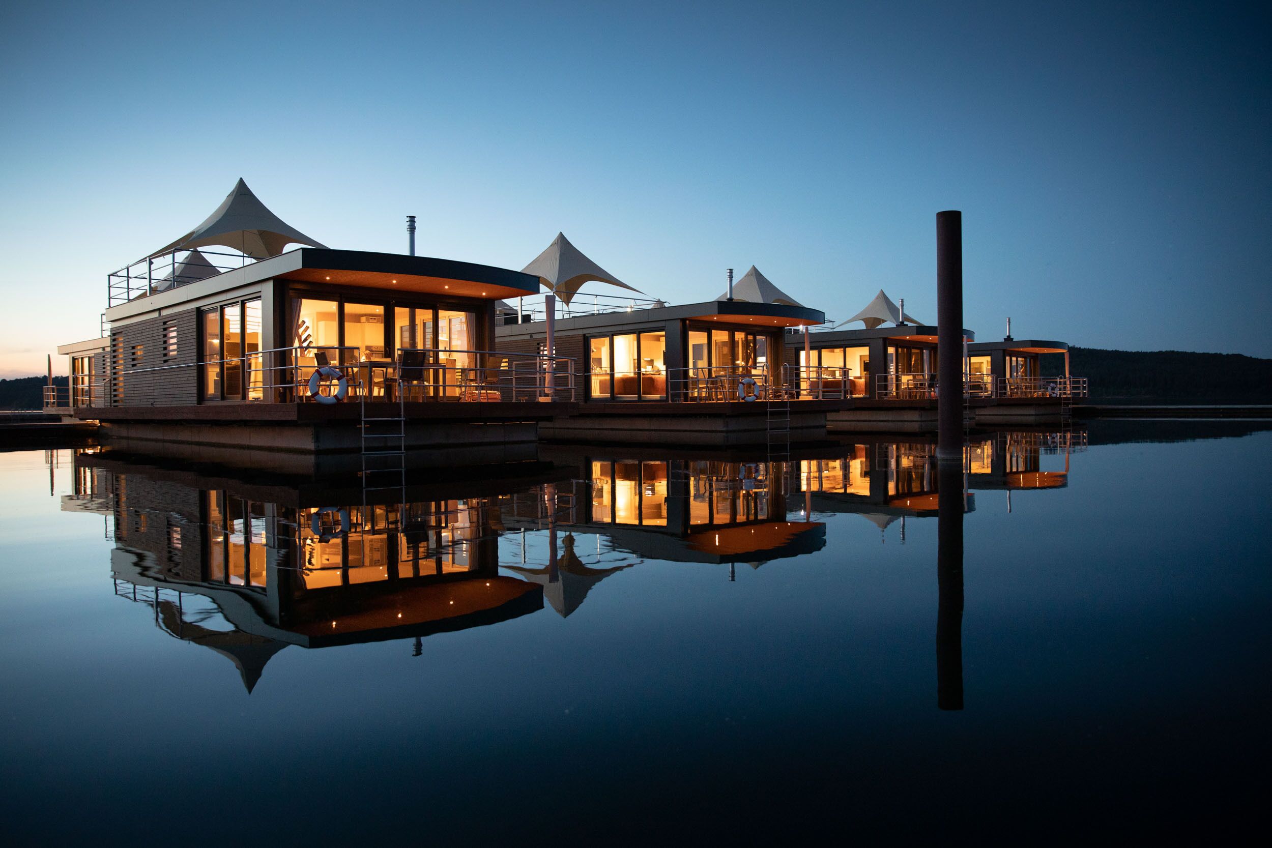 A waterfront property with multiple connected buildings, large umbrellas, and a calm reflective water surface.