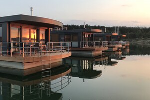 A series of floating structures with outdoor seating areas and a view of the sunset over the water.