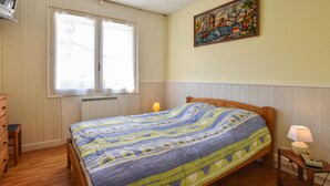 Une chambre avec un lit en bois, une fenêtre à vitre dépolie, un radiateur, une table de chevet avec une lampe et un tableau accroché au mur.