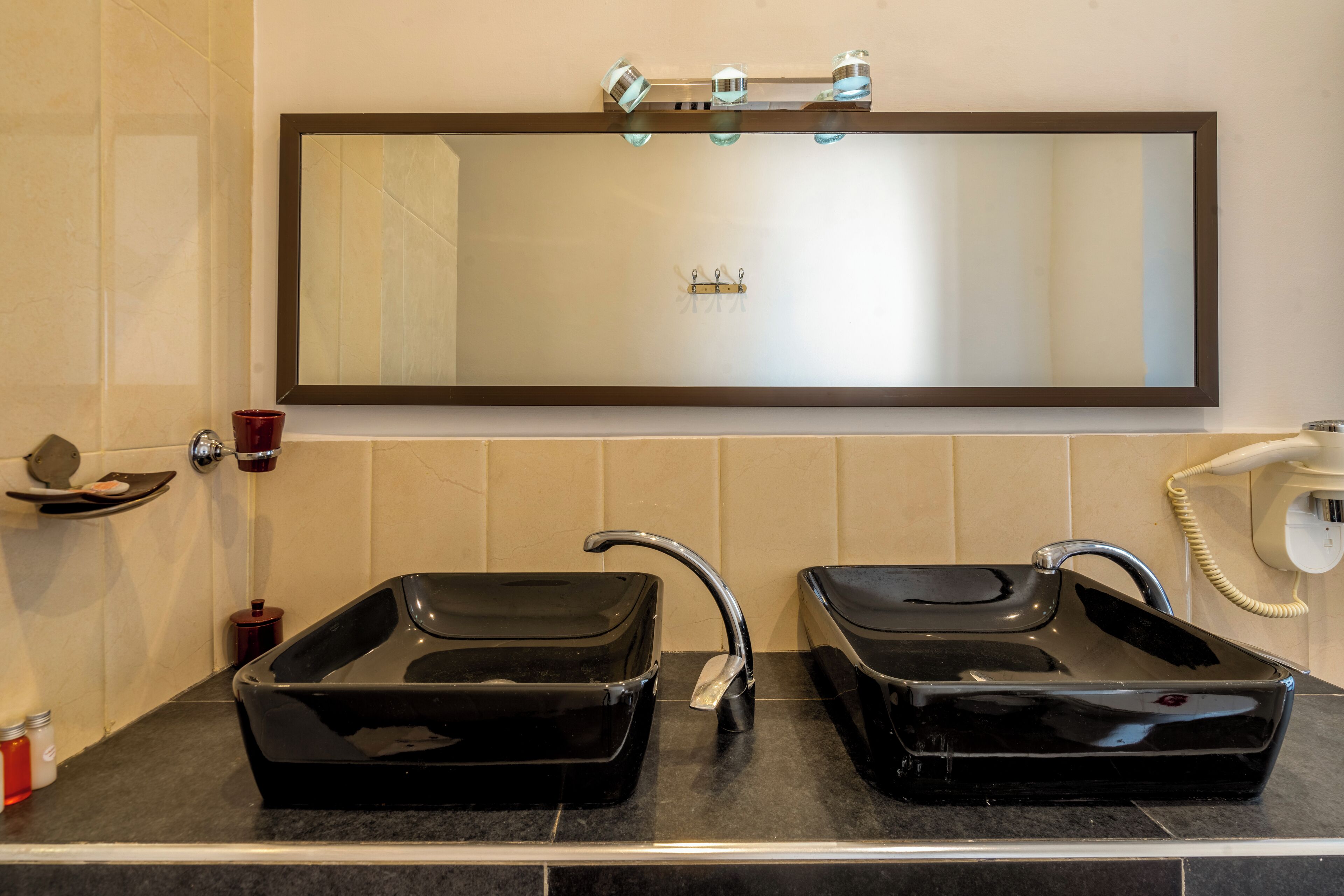 Un baño con dos lavamanos negros, un espejo grande y un perchero para toallas.