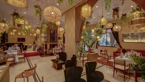 Un hall d’hôtel spacieux, doté de plusieurs coins salon, de lampes suspendues en osier et de plantes en pot.