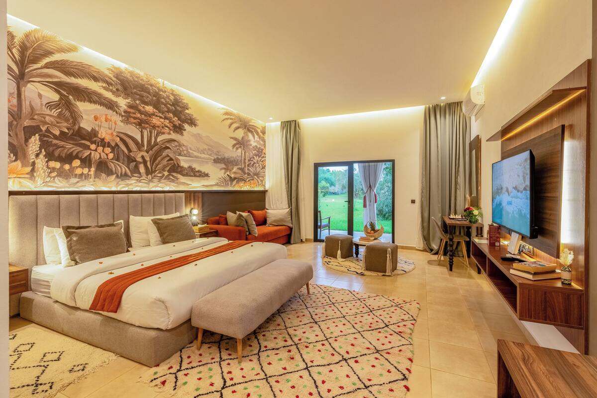 Een moderne slaapkamer met een groot bed, een televisie en een muurschildering van een tropisch landschap.