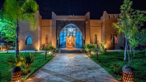 Une entrée bien éclairée, avec une arche centrale, un chemin pavé et une végétation luxuriante tout autour.