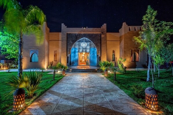 A well-lit entrance with a central archway, a paved pathway, and surrounding greenery. - Taj Atlas Wellness Boutique Hotel & Spa (Sidi Badhaj)