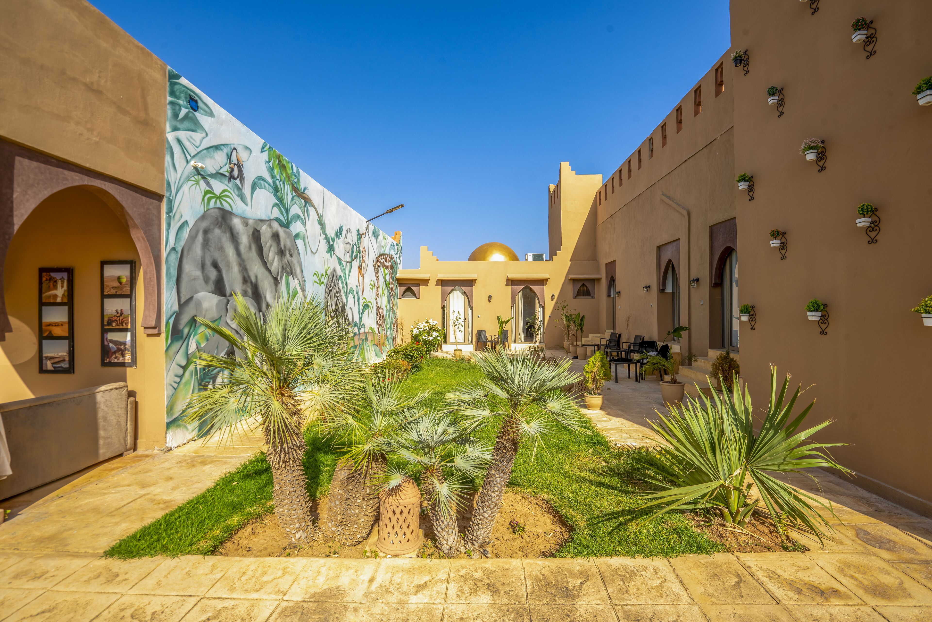 A courtyard with palm trees, a mural, and a building with a dome and arches.
