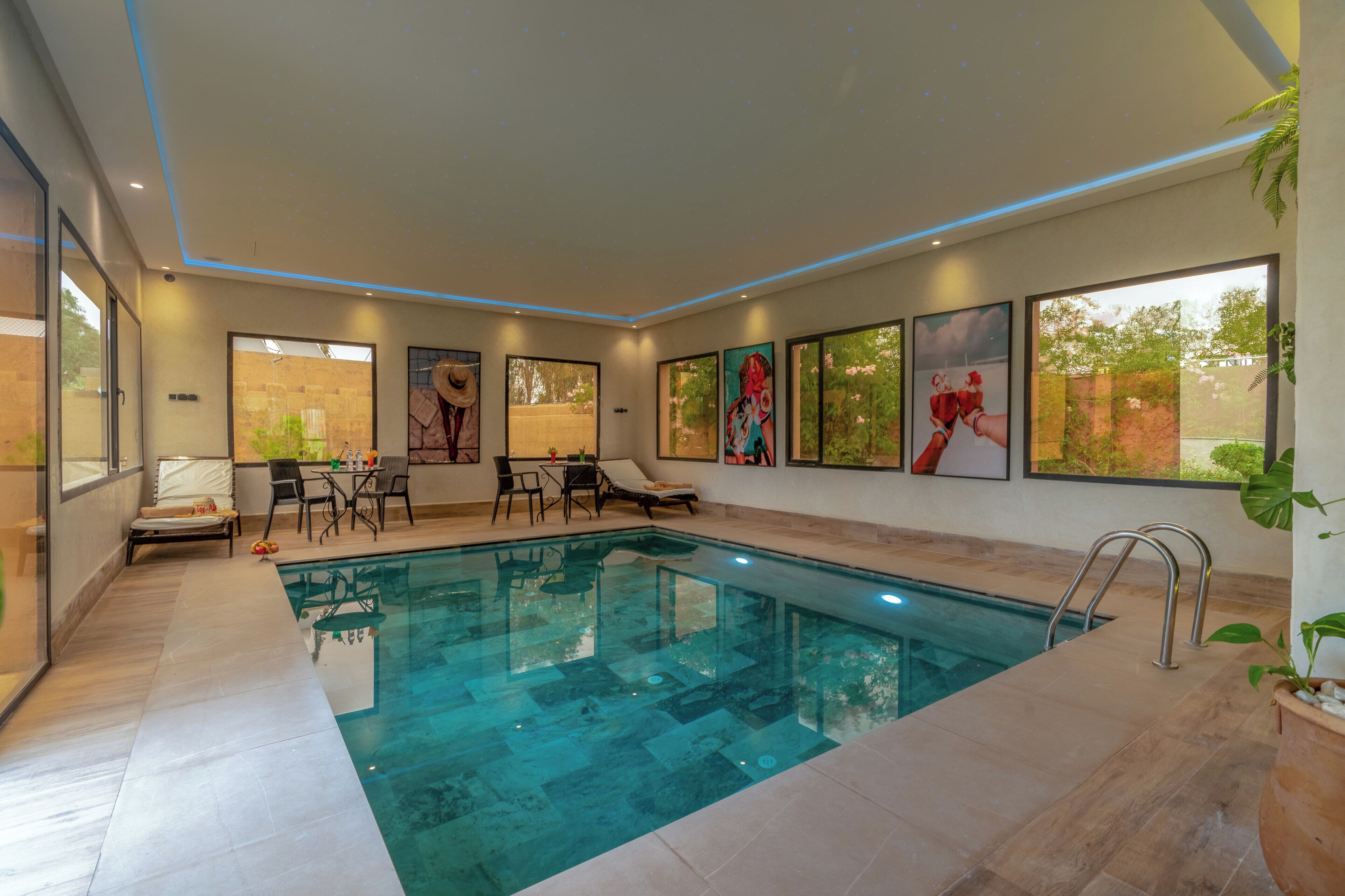 An indoor swimming pool with clear blue water, surrounded by lounge chairs and a table.