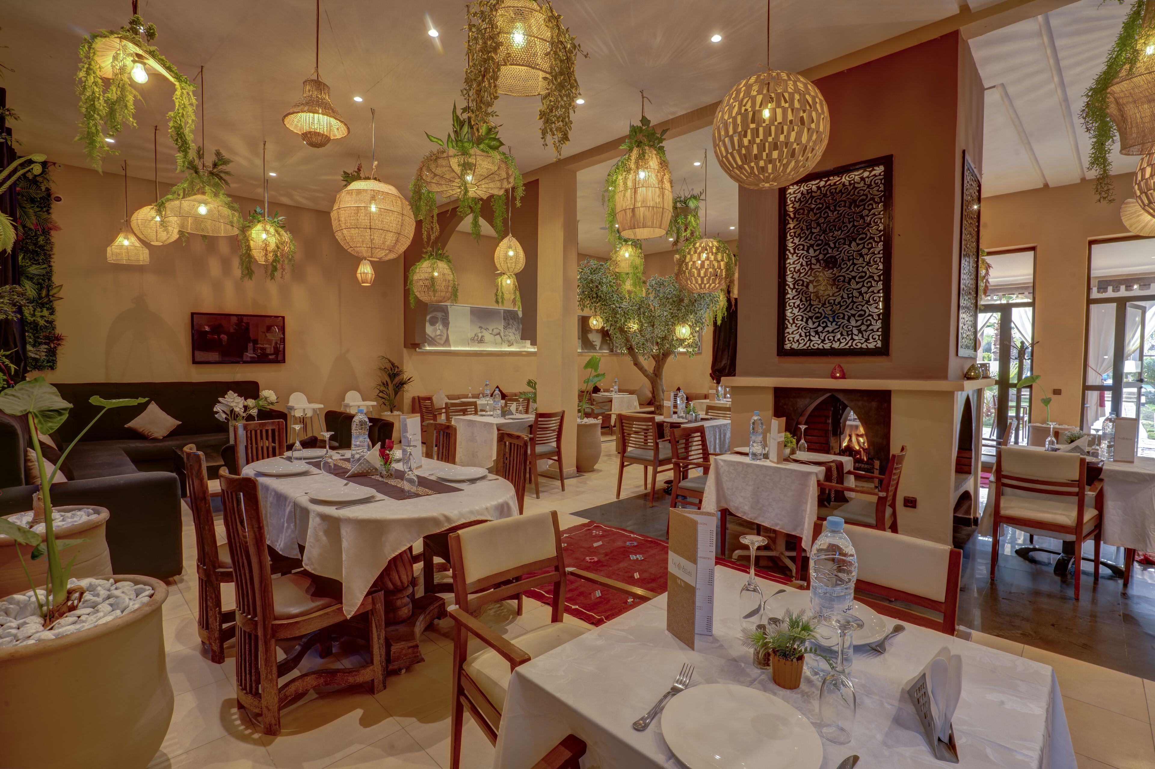 A restaurant with multiple tables, hanging plants, and a fireplace.