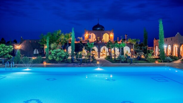 Une piscine avec une mosquée en arrière-plan, entourée de verdure et éclairée par un éclairage d’ambiance.