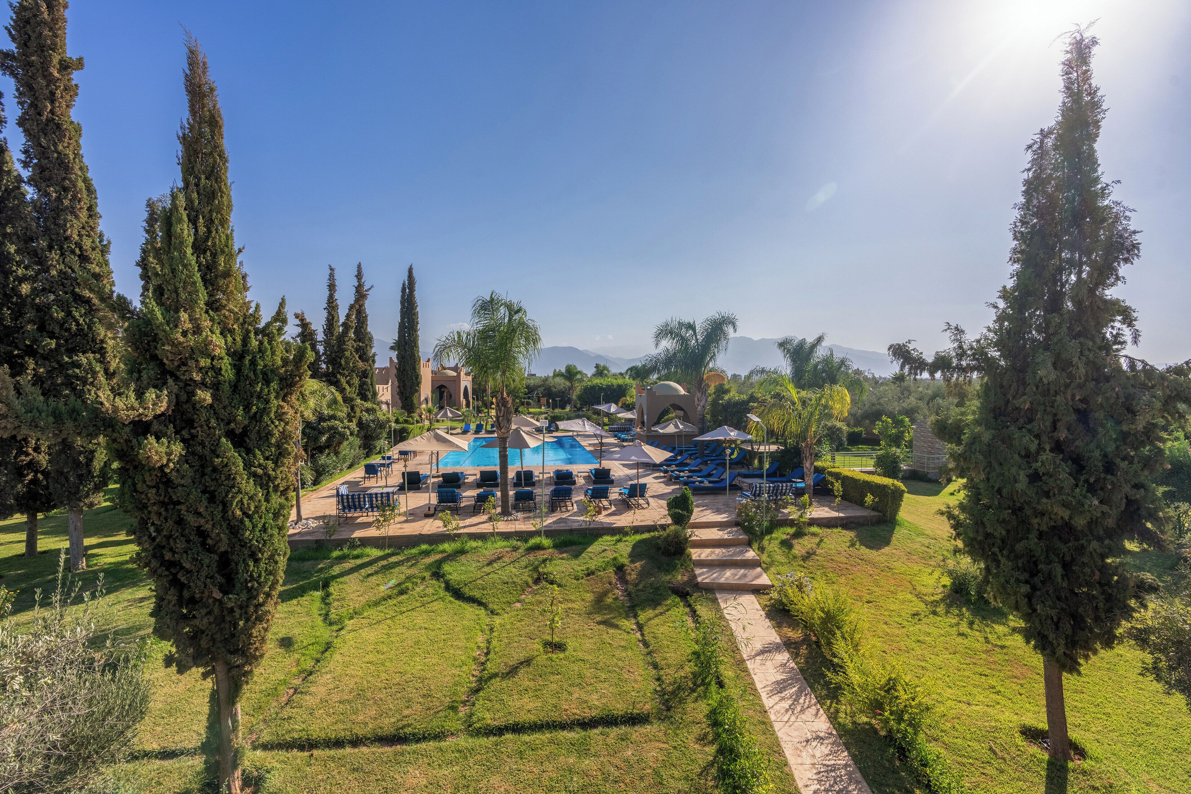 A resort with a swimming pool, lounge chairs, and a view of distant mountains.