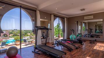 Un gimnasio amplio en casa con cinta de correr, pelotas de ejercicio y pesas. Grandes ventanales ofrecen vistas a una piscina y follaje.
