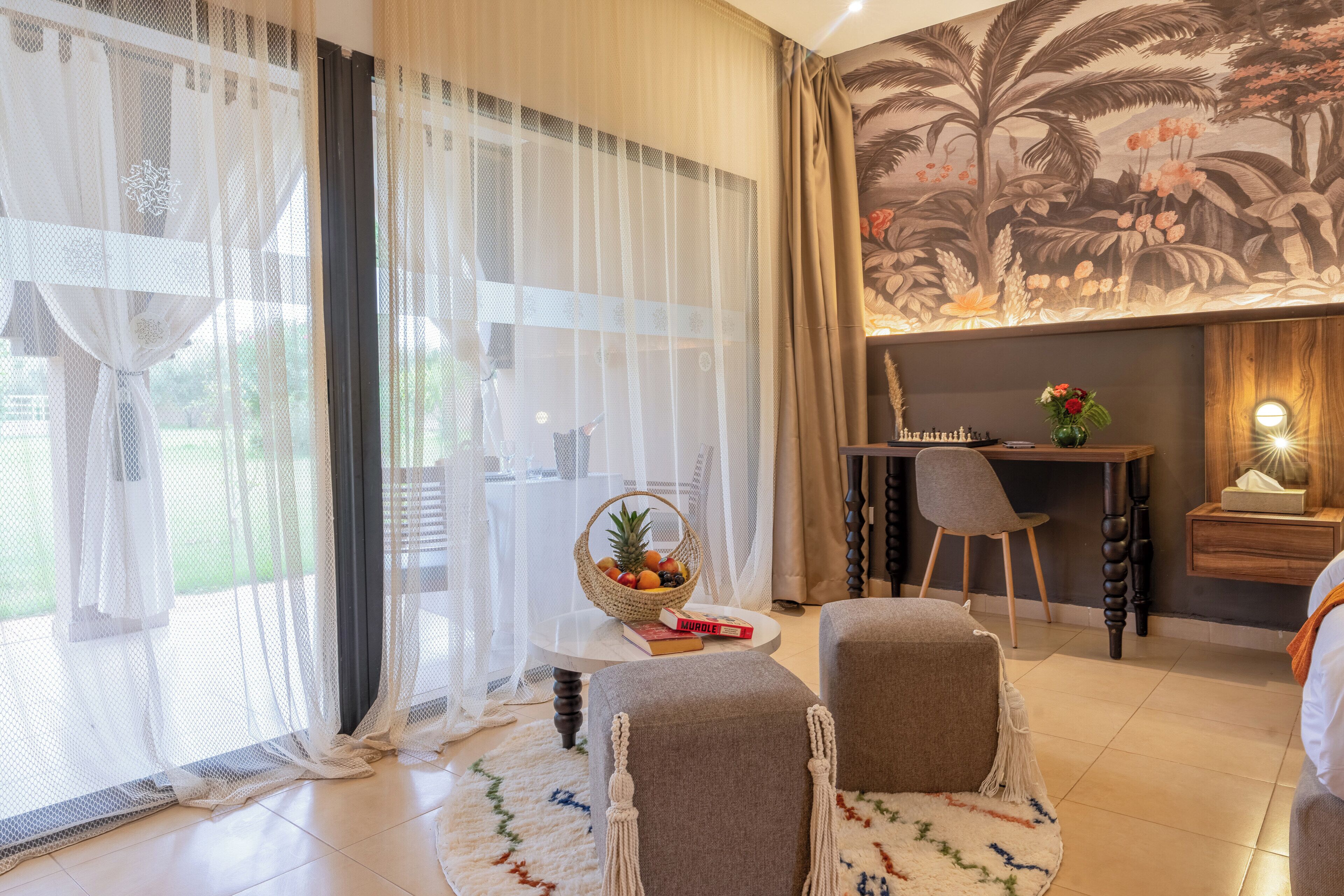 A room with a large window, a dining area with a table and chairs, a small sofa, and a decorative wall mural.