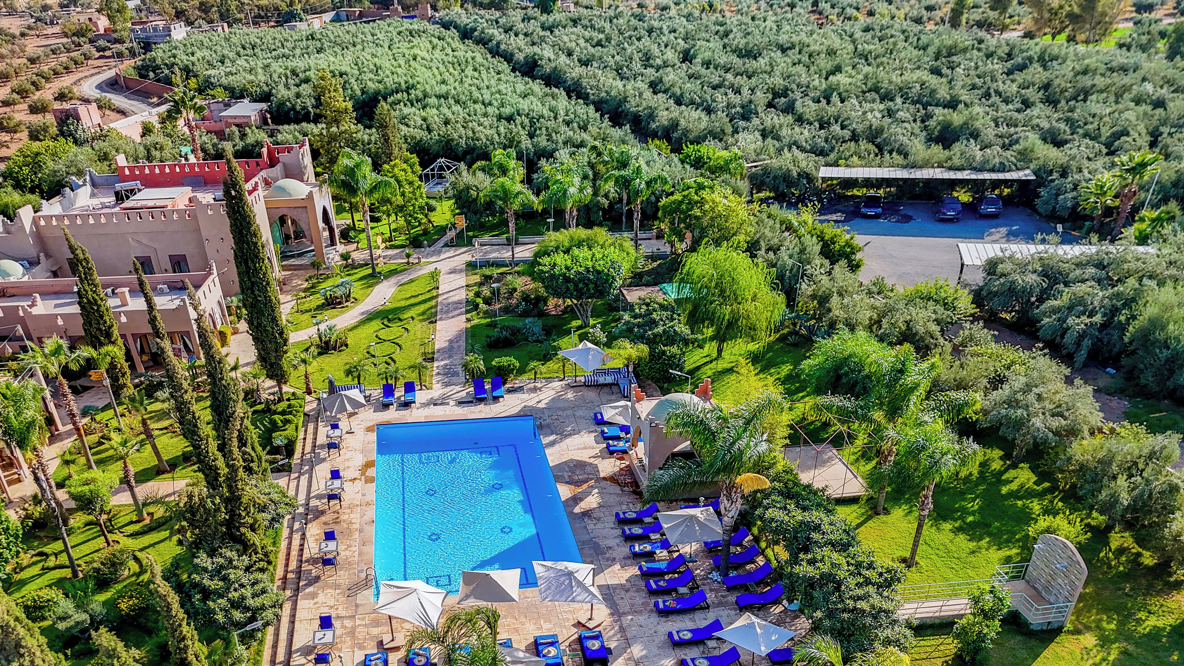 An aerial view of a resort with a swimming pool, sun loungers, and a landscaped garden.