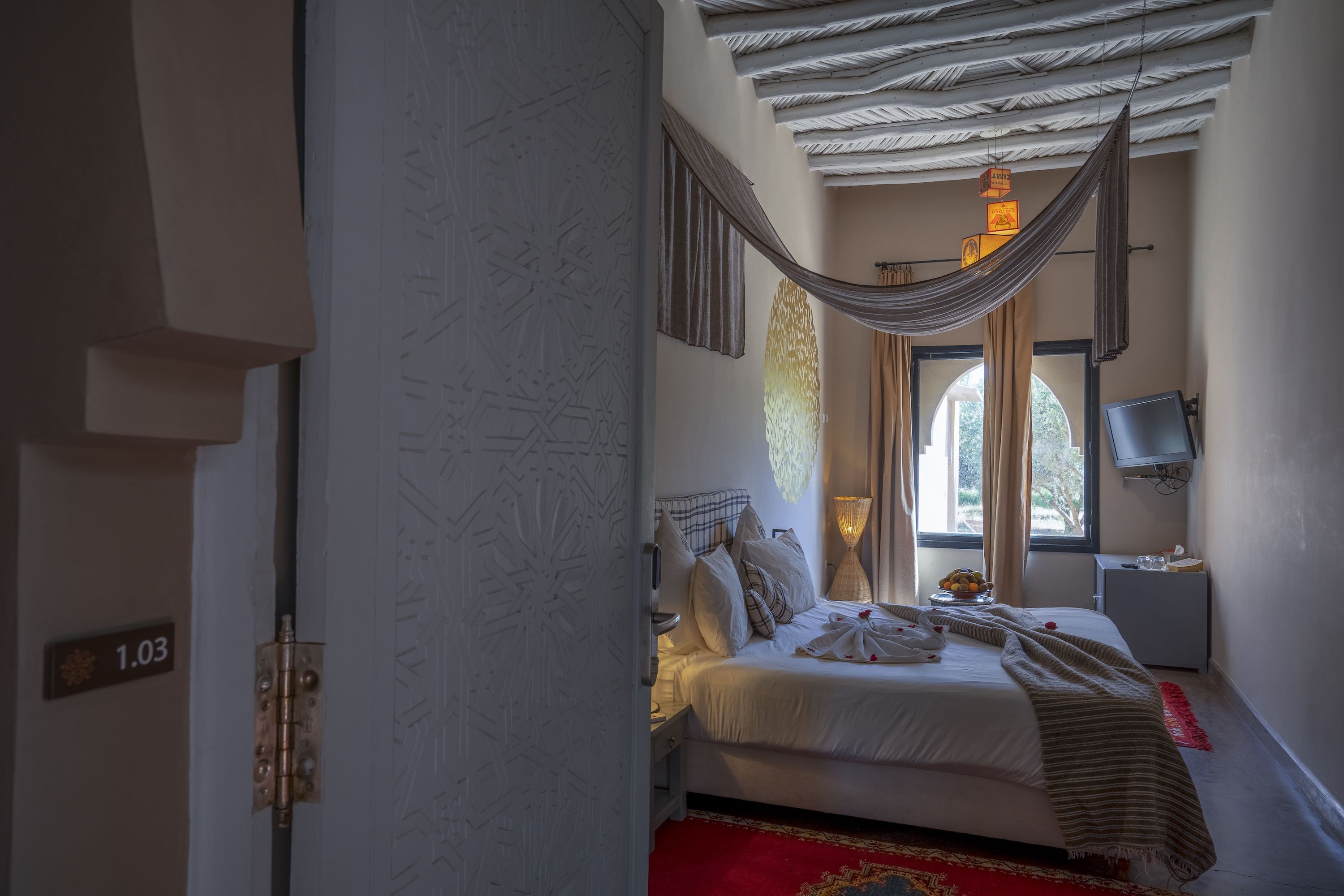 A bedroom with a bed, a nightstand, a TV, and a window with curtains.