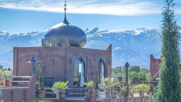 A building with a dome and arched windows, surrounded by potted plants and a mountainous backdrop.