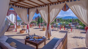 Un espace extérieur aménagé avec des sièges et une table préparée pour le petit-déjeuner, offrant une vue sur une piscine et des montagnes.