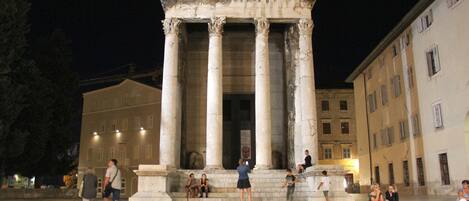 A classical building with columns, a central staircase, and a surrounding urban environment at night.