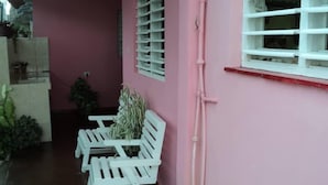 Um edifício rosa com persianas brancas, um banco branco e plantas em vasos.